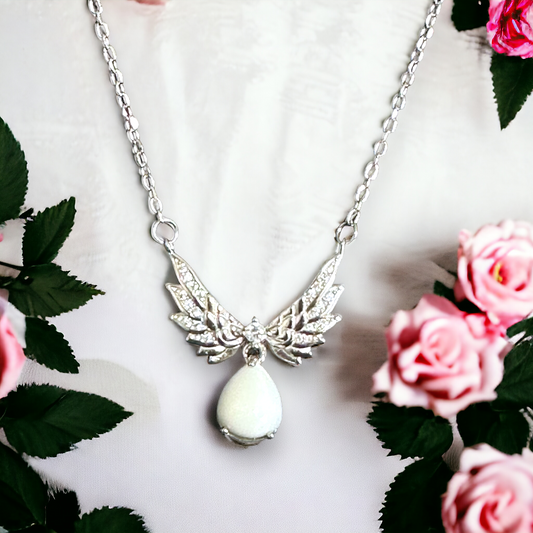 Closeup of Heavenly Embrace sterling silver necklace featuring angel wings encircling a pear-shaped white breastmilk stone, symbolizing protection and the pure bond between mother and child.