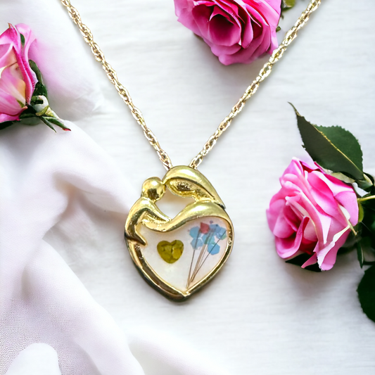 Close-up of Mother's Love gold pendant featuring a heart with a mother and child silhouette, accented with a unique bouquet made from hair and sparkles, and a small sparkle heart beside the bouquet, showcasing intricate details of breastmilk/cremation ash jewelry.