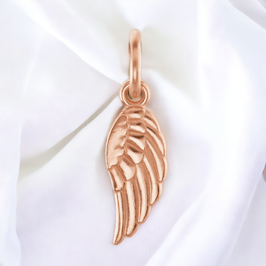 Rose gold angel wing charm by Posh Mommy, elegantly draped on a silky background, highlighting its polished surface and intricate feather details.