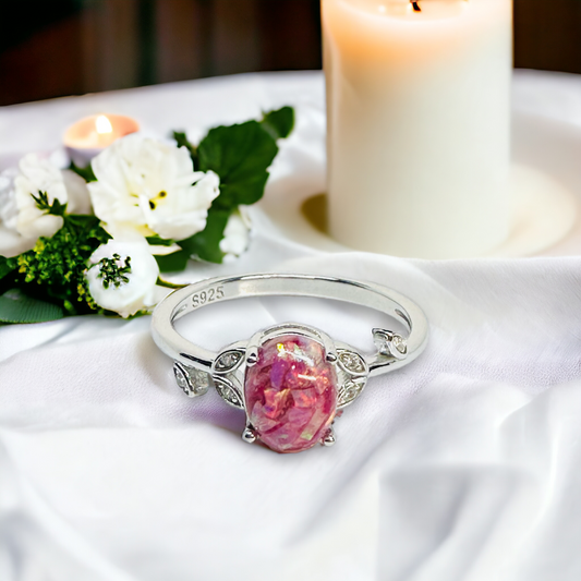 Close-up of Flora Petite Floral Ring in Silver on a table, showcasing an Aurora crushed opal cremation stone, flanked by sparkling cz leaves, symbolizing everlasting beauty and memory.