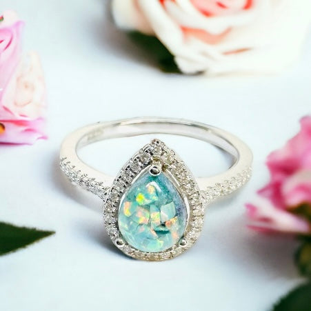 Close-up of Precious Drop Halo Pear Ring in Sterling Silver on a table, featuring a central cremation stone made of Neptune crushed opal encircled by sparkling cz stones, symbolizing a celestial connection.